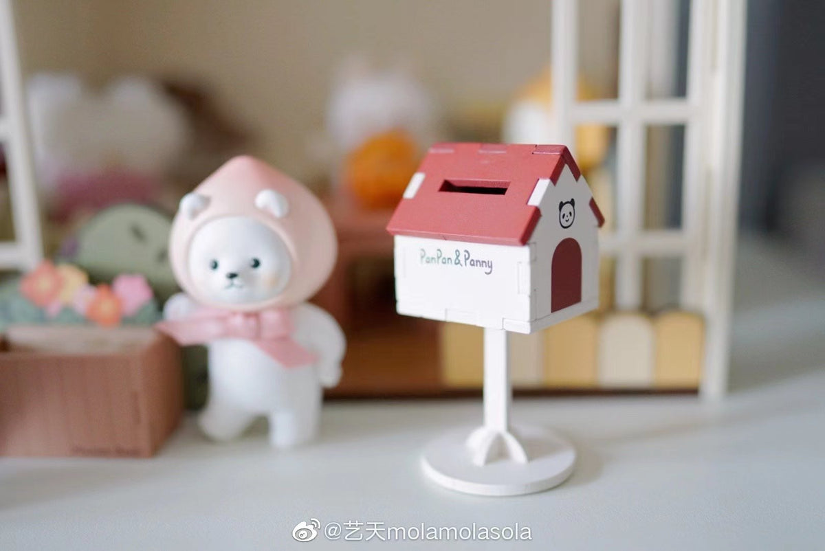 Pink-hooded collectible figure beside a PanPan & Panny mailbox in a miniature home scene